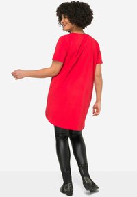 Tunic rossa a maniche corte con pieghe sul retro, abbinata a leggings neri in pelle sintetica e stivaletti neri con borchie.