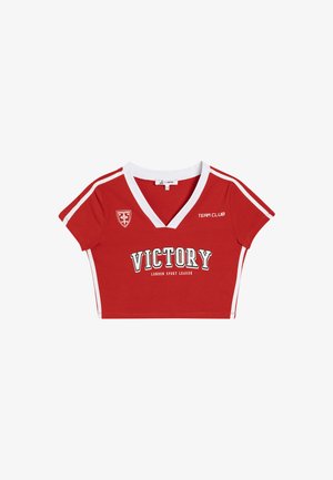 Rode cropped T-shirt met witte V-hals, korte mouwen en zijstrepen. Voorzien van de opdruk "VICTORY" en een badge op de borst.