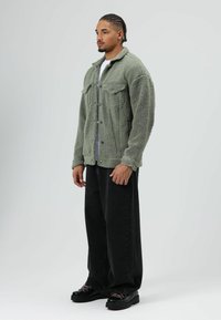 Green fuzzy jacket with a soft texture, collar, and front button closure. Paired with loose black jeans and chunky black shoes.