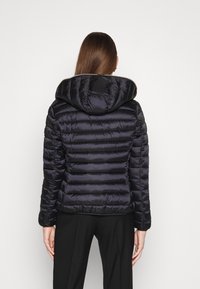 Sort dynejakke med hætte, der har et horisontalt quiltet design og skinnende materiale. Jakken har en tætsiddende silhuet og lange ærmer.