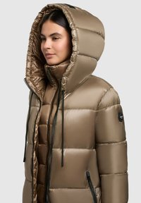 Pufferjack in metallic taupe, met een grote capuchon, een ritssluiting aan de voorkant en zwarte trekkoorden. Glad exterieur met zijzakken en logo.