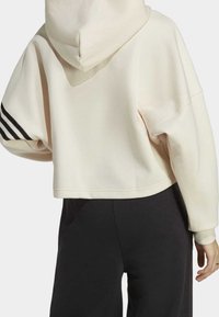 Kremowa krótka bluza z kapturem, z czarnymi paskami na lewym rękawie. Wykonana z miękkiego materiału o luźnym kroju.