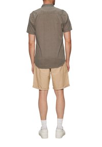 Korte mouwen, knoopjesoverhemd in donkergrijs, met een patroon, gecombineerd met lichtbeige shorts. Het model draagt witte sneakers en sokken.