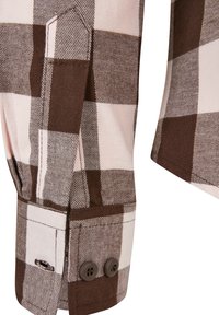 Manica di una camicia di flanella a quadri marrone e beige, con chiusura a bottone e cuciture a contrasto su un tessuto morbido.