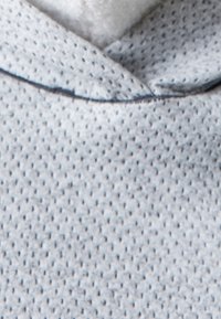 Ljust blått, texturerat tyg med ett bikake-mönster, med en mjuk, vit fleecefoder vid halsringningen och huvan.