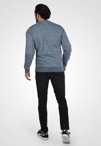 Pulover tricotat de culoare bleu deschis, cu mâneci lungi, guler rotund, finisaj texturat, asociat cu blugi negri și adidași negri cu accente crem.