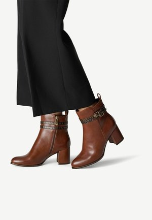 Bottes chevilles en cuir marron avec un bout arrondi, un talon bloc et une sangle décorative avec une boucle. Texture lisse avec une fermeture éclair sur le côté.