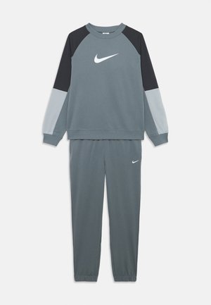 Survêtement Nike gris avec sweat-shirt à manches longues en blocs de couleurs et pantalon de jogging assorti, tous deux arborant des logos Swoosh Nike blancs.