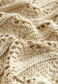 Pletený šál v světle zlaté barvě, zdobený otevřeným vzorem s texturovaným povrchem. Měkká příze s jemným leskem, složená na neutrálním povrchu.