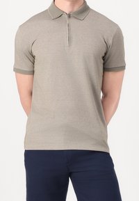Polo beige avec un col zippé, des manches courtes et un col et des poignets texturés. Le tissu est lisse et léger.
