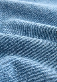 Tessuto denim di colore azzurro chiaro con una trama liscia e una leggera tessitura diagonale, che mette in evidenza morbide pieghe e grinze per maggiore profondità.