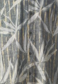 Button-up shirt featuring a textured fabric with a gray background, abstract floral pattern in white and yellow, and dark buttons.
