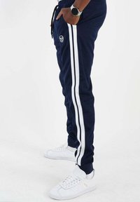 Marineblauwe joggingbroek met witte zijstrepen, een trekkkoord in de taille en een logo-detail. Gecombineerd met witte sneakers met een textuurdesign.