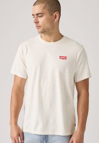 T-shirt en coton beige clair à manches courtes, avec un petit logo rouge Levi's sur la poitrine et une coupe droite.