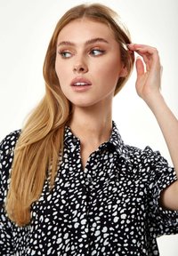 Black shirt with a white speckled pattern, featuring a collared neckline and short sleeves, set against a light background.