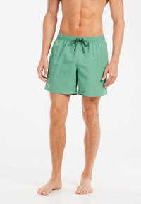 Shorts de bain verts en tissu léger, dotés d'une taille élastique avec un cordon noir et de poches latérales.