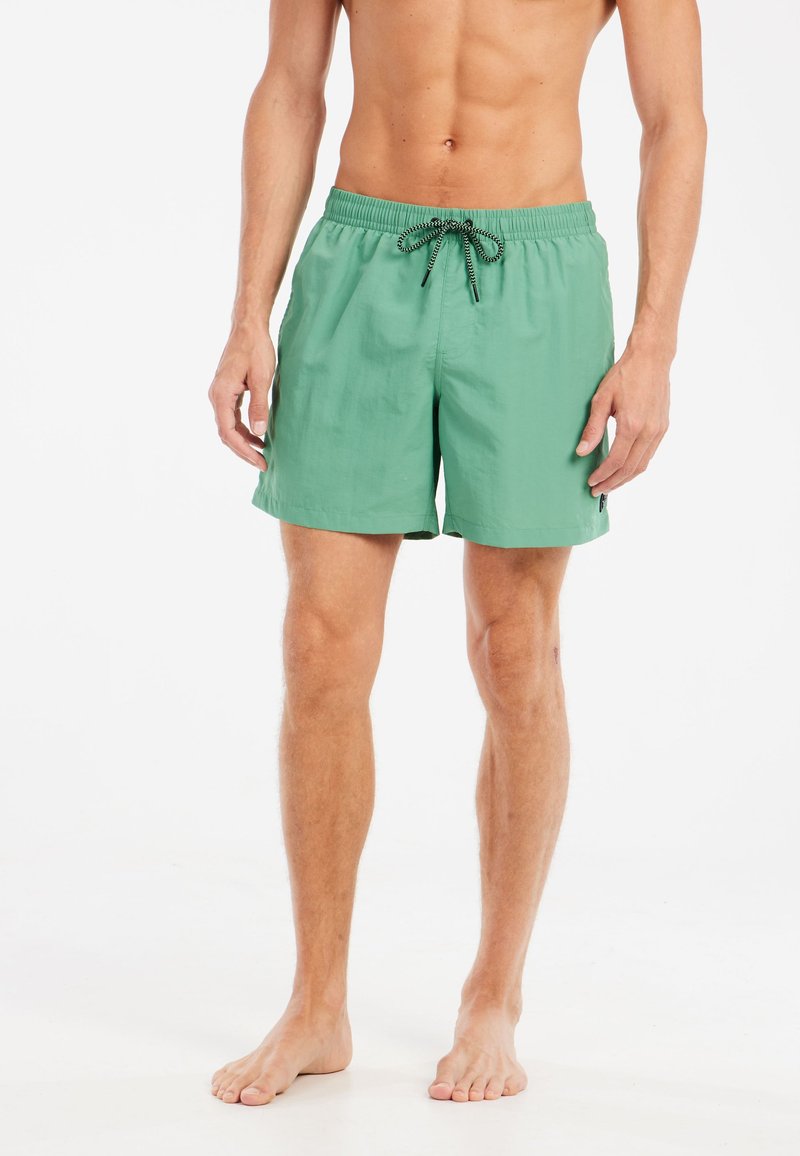Shorts de bain verts en tissu léger, dotés d'une taille élastique avec un cordon noir et de poches latérales.