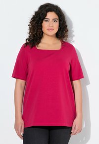 T-shirt fuchsia avec un col carré, des manches courtes et une coupe ample. Fabriqué en tissu doux avec une texture lisse. Porté avec un pantalon noir.