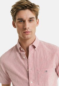 Kurzarmhemd mit rot-weißen Streifen, ausgestattet mit einem Kentkragen, einer Brusttasche und einem kleinen gestickten Logo auf der Tasche.