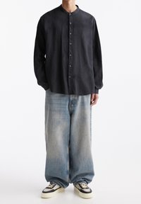 Zwarte langemouwen knoopshirt met een ronde hals, gedragen met lichtblauwe, loszittende spijkerbroeken en zwart-witte sneakers.
