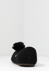 Slipper nera in feltro con punta arrotondata, superficie textured e un pompon sul retro. Suola piatta per il comfort.