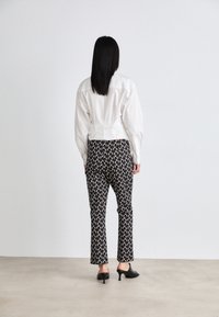 White, cropped button-up shirt paired with patterned, fitted black pants featuring a leaf design. Worn with black open-toe heels.