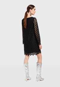 Mustat mekko, jossa on sydämenmuotoisia aukkoja, pitkät hihat ja aallotettu helma. Yhdistetty polvipitkiin hopeakorkoisiin saappaisiin. Siloinen ja kiiltävä pinta.