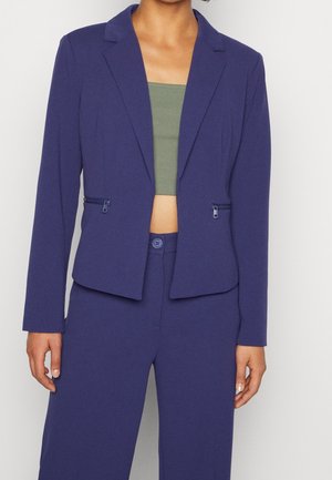 Blazer blu navy con un design strutturato, risvolti a notched e tasche con zip. Tessuto leggero con una texture liscia e vestibilità su misura.