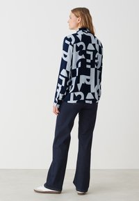 Langärmlige gemusterte Bluse mit einem navyblauen und hellblauen abstrakten Design. Kombiniert mit dunkelblauen, ausgestellten Jeans und weißen Sneakers.