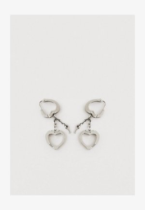 Stříbrné kovové náušnice srdcového tvaru s řetízkovým vzorem. Náušnice mají uzávěr na zavěšení pro bezpečné nošení.