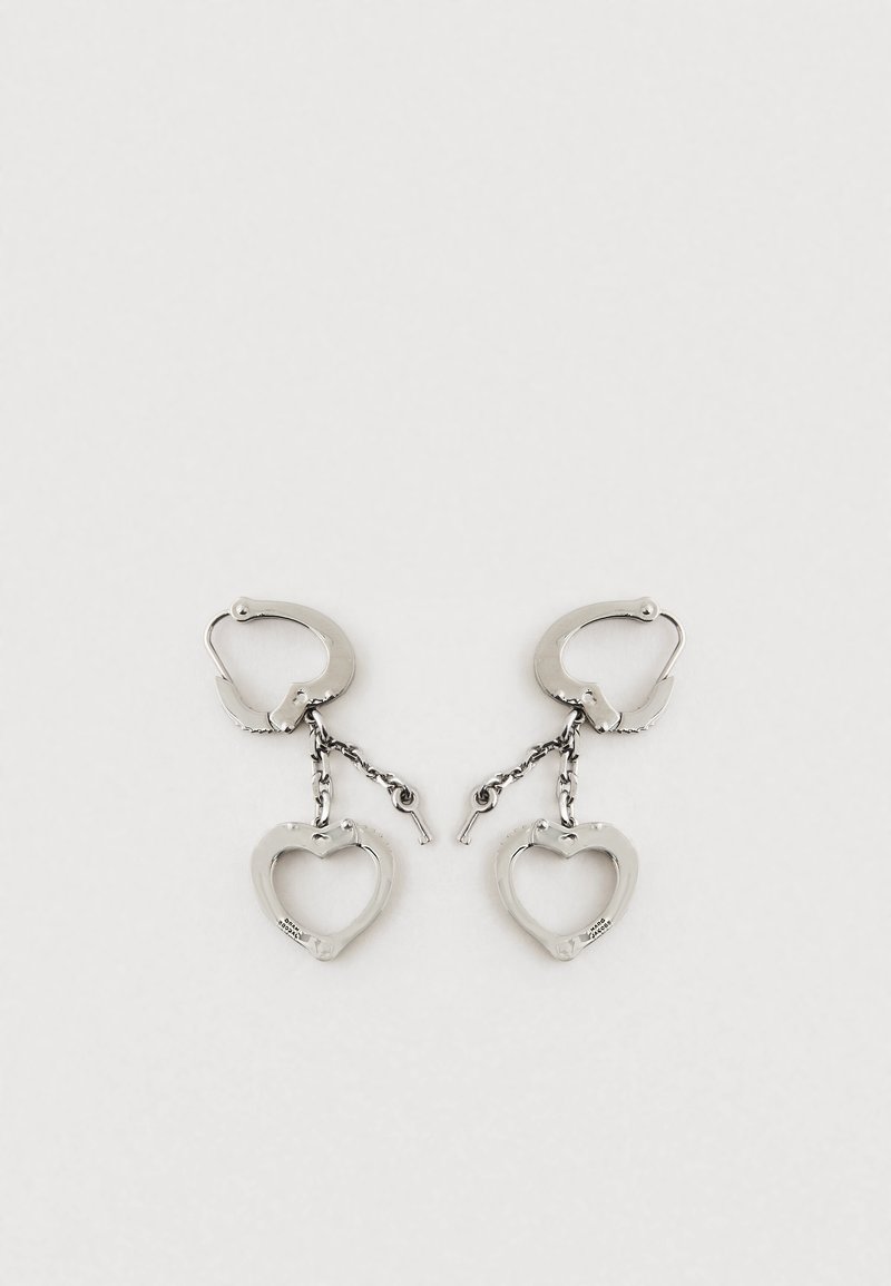 Strieborné kovové náušnice so srdcovým dizajnom a reťazovým spojom. Náušnice majú mechanizmus na uzatváranie na bezpečné nosenie.