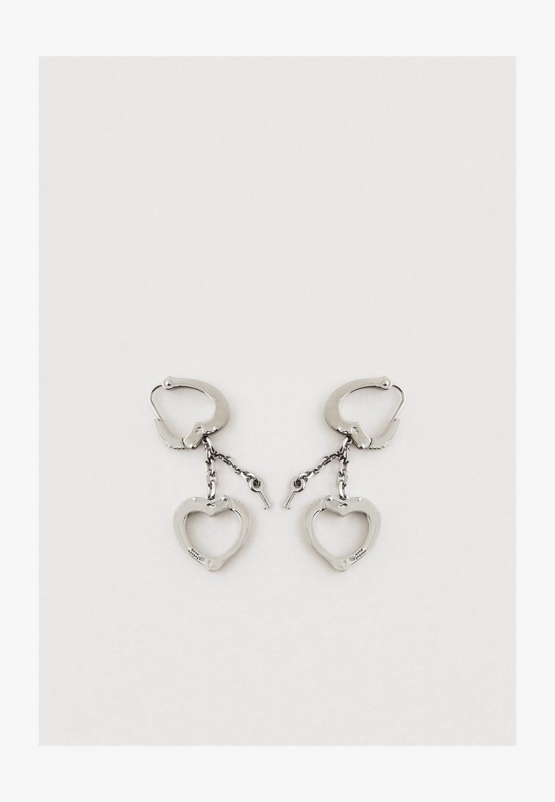 Strieborné kovové náušnice so srdcovým dizajnom a reťazovým spojom. Náušnice majú mechanizmus na uzatváranie na bezpečné nosenie.