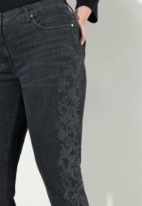 Jeans de mezclilla negra con un patrón floral hecho de cuentas y remaches a lo largo del lateral, con un diseño ajustado y bolsillos estándar.
