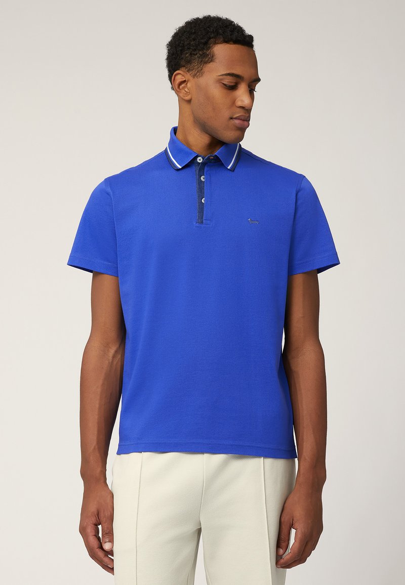 Polo blu con colletto a contrasto navy e pattina a tre bottoni. Maniche corte e tessuto strutturato. Dettaglio con logo piccolo sul petto.