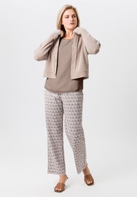 Beige cropped cardigan met een gestructureerde brei, over een taupe top. Brede broek met een bruin geometrisch patroon. Bruine sandalen maken de look compleet.