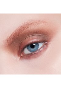 Gros plan sur un œil avec un iris bleu clair, un eyeliner subtil et un fard à paupières brun chaud. La peau a une texture lisse et légèrement réfléchissante.