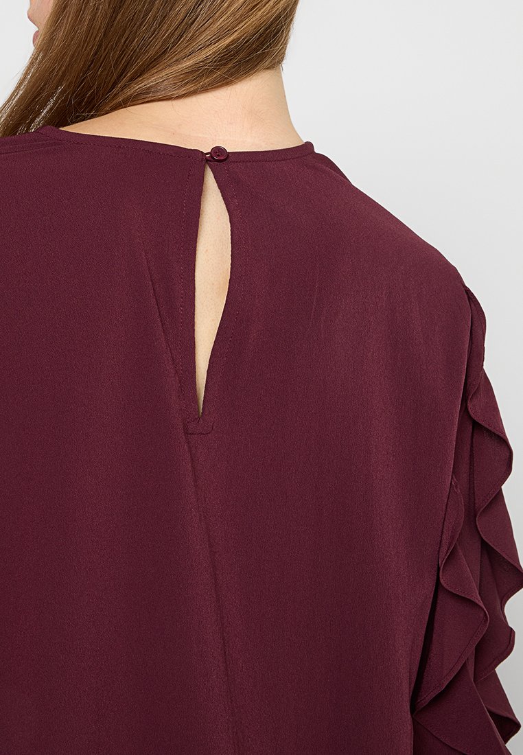 Bordeauxblouse met een sleutelgatdetail aan de achterkant en een knoopsluiting, van zacht materiaal, met gerimpelde mouwen die textuuraccenten bieden.