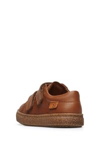 Scarpa in pelle marrone con taglio basso, due cinturini in velcro, dettagli perforati e suola in gomma testurizzata. Presenta un'etichetta con logo sul tallone.