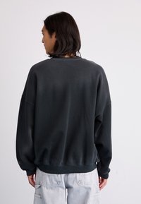 Felpa grigia scura con un taglio comodo, polsini e orlo a coste. Tessuto morbido e testurizzato, con spalle scese e design minimalista.