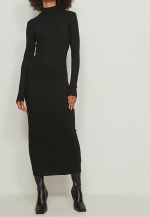 Czarna prążkowana sukienka z długim rękawem, z wysokim dekoltem, dopasowanym krojem i pełną długością, zestawiona z czarnymi botkami na obcasie.