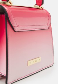 Růžová kabelka s přechodem barev, černým lemováním, zlatou sponou a značkovou destičkou ALDO na přední straně, zobrazená v detailním záběru.