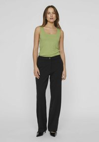 Jasnozielony top na ramiączkach z kwadratowym dekoltem, zestawiony z czarnymi, dopasowanymi spodniami i czarnymi wysokimi obcasami, o gładkiej, matowej fakturze.