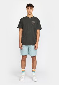 Grijze t-shirt met korte mouwen en een kleine bergafbeelding, gecombineerd met lichtblauwe shorts en witte sneakers, voorzien van meerkleurige gestreepte sokken.