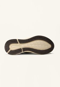 Zool van een beige en zwarte rubberen schoen met profielpatroon en zichtbare "OHSKO" branding op het hielgebied.