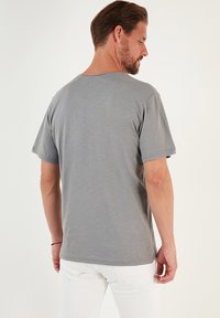 Siva majica s kratkimi rokavi in okruglim ovratnikom, izdelana iz mehkega materiala, z ohlapnim krojem in vidnimi šivi ob robu in rokavih.