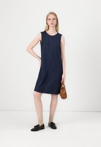 Μπλε τζιν αμάνικο φόρεμα με κεντρική ραφή, μήκους μέχρι το γόνατο, με λεία υφή, συνδυασμένο με καφέ τσάντα και μαύρα παπούτσια.