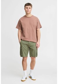Brun bomulds t-shirt med korte ærmer, kombineret med olivengrøn cargo shorts med sidelommer. Afsluttet med hvide og grønne sneakers.