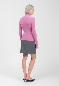 Maglione a collo alto a costine rosa aderente abbinato a una gonna grigia con motivi a pois bianchi. La modella indossa mule nere.