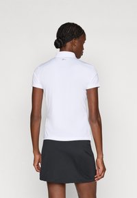 Camisa polo branca com um colarinho pequeno, mangas curtas e um bainha reta, combinada com uma saia preta. Tecido liso com detalhes subtis.