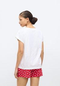 Άσπρο βαμβακερό μπλουζάκι με κοντά μανίκια, συνδυασμένο με κόκκινα σορτς με λευκά σχέδια καρδιών. Άποψη από πίσω, που παρουσιάζει άνετα ρούχα για το σπίτι.